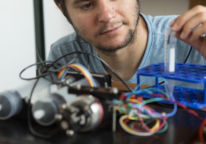 engineer works on an open sensor with different colored wires in the foreground