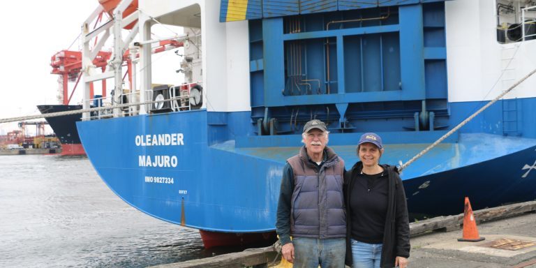 IMG_2879 Two scientists stand in front of the stern of a ship with the name Oleander in white visible on the ship.